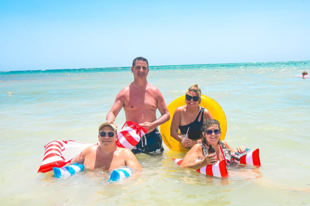 Four people standing together in the shallow, murky water at Blue Water Beach Club, enjoying a fun moment during their beach day