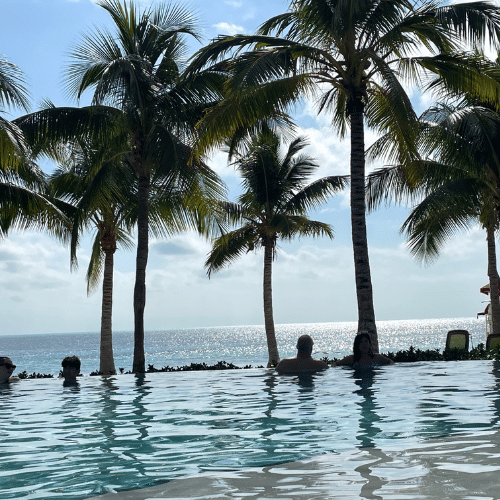 Infinity pool at CocoCay Beach Club with palm trees and ocean views, a relaxing spot to enjoy the best cruise cocktails.