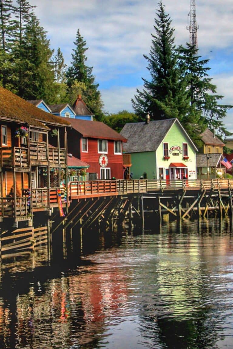 Colorful wooden buildings on stilts lining a forested creek in Ketchikan, Alaska.