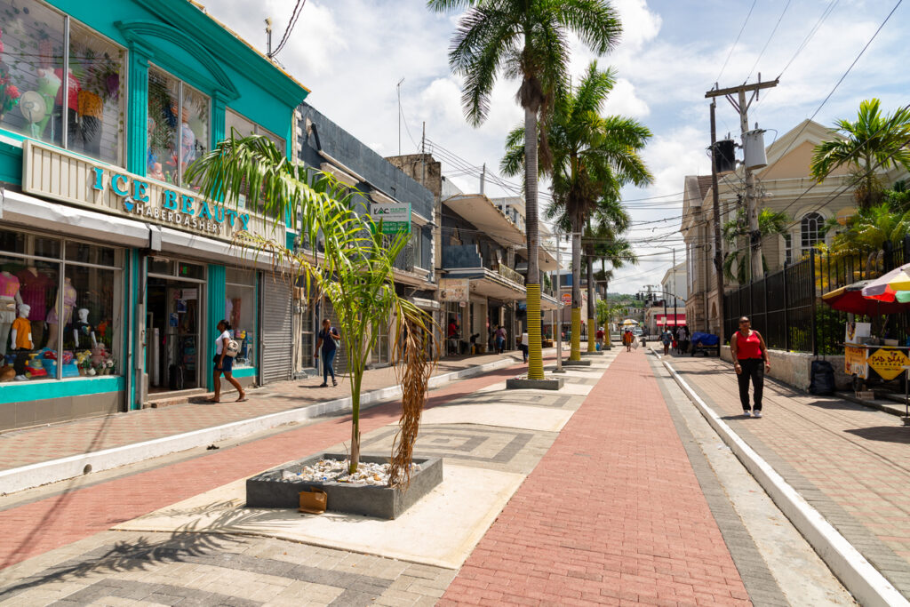 Pedestrian walkway on the Hip Strip in Montego Bay, Jamaica, with colorful storefronts, palm trees, and visitors shopping on a sunny day