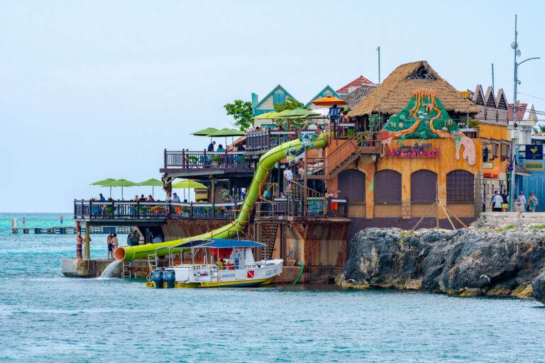 People enjoying the sun and ocean views at Jimmy Buffett’s Margaritaville Montego Bay on the Hip Strip, with cliffs and Caribbean water in the background