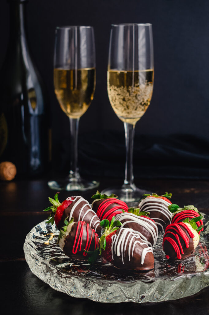 Close‑up of chocolate‑covered strawberries on a small plate beside two champagne glasses, a romantic treat for an anniversary celebration cruise.