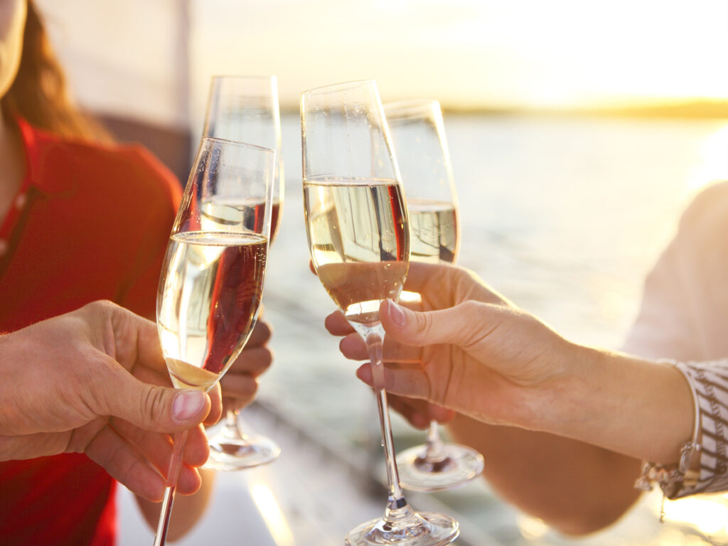 Close‑up of four hands holding champagne glasses in a celebratory toast at sunset, capturing a romantic moment during an anniversary celebration cruise.