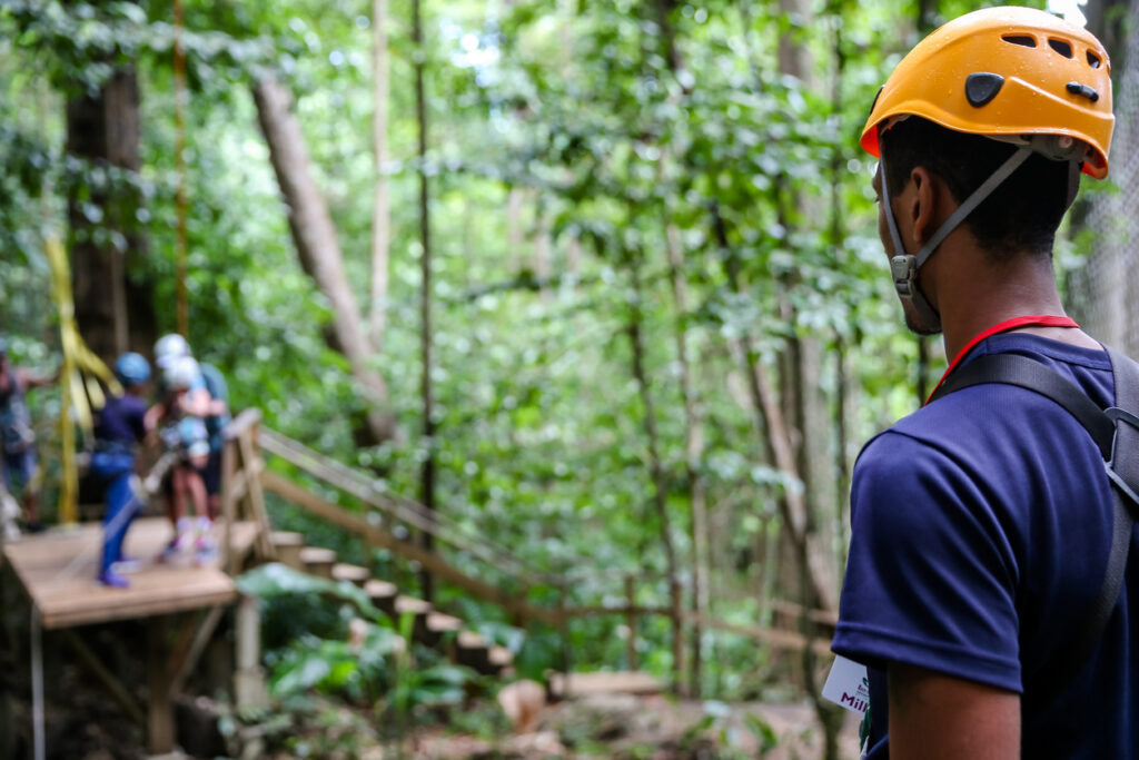Zip‑line guide standing on a treetop platform, watching guests on the course and preparing for the next rider