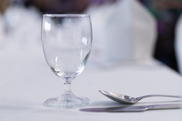 Close‑up of a wine glass and silverware on a white tablecloth, representing the elevated dining experience of coastal kitchen on royal caribbean.
