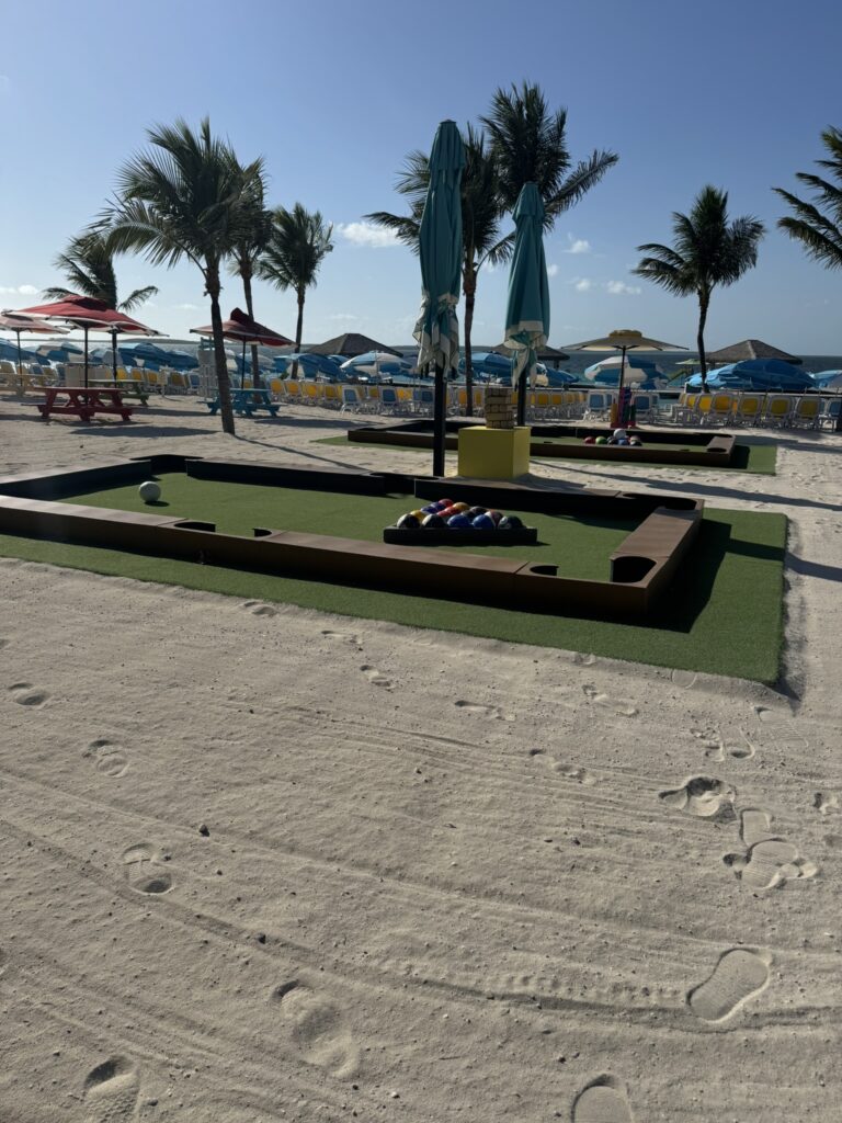 A life‑size outdoor billiards-style game played with soccer balls on a turf table near the beach at CocoCay, with lounge chairs, umbrellas, and palm trees in the background.
