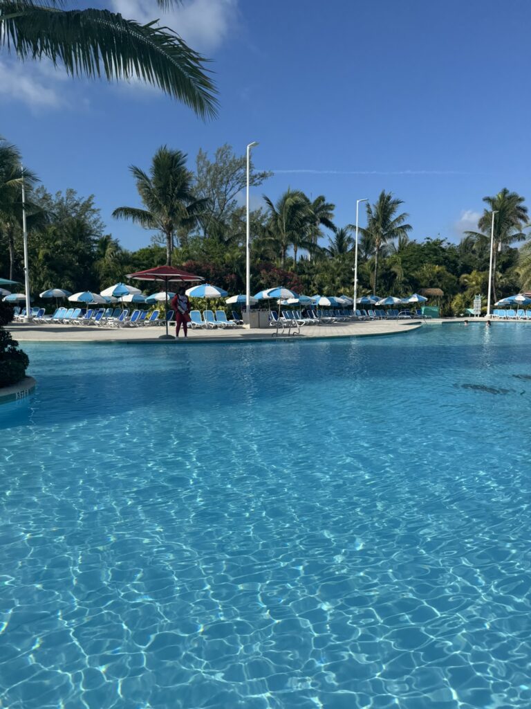 Oasis Lagoon at CocoCay with guests swimming and relaxing in the large freshwater pool, surrounded by palm trees, loungers, and bright island scenery.