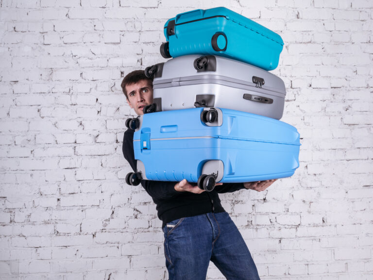 Unhappy man struggling to hold three heavy suitcases, visually emphasizing the importance of understanding cruise luggage rules and the benefits of packing light before embarkation.