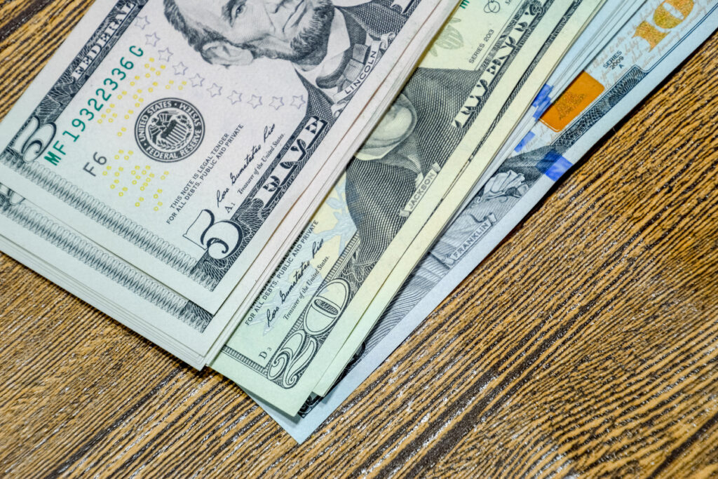 Stacks of U.S. bills on a wooden surface, representing the costs and considerations involved in cruise tipping etiquette.