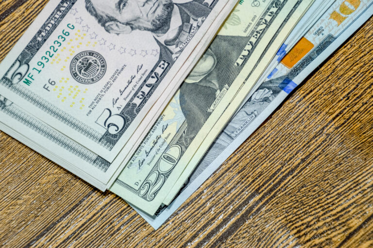 Stacks of U.S. bills on a wooden surface, representing the costs and considerations involved in cruise tipping etiquette.