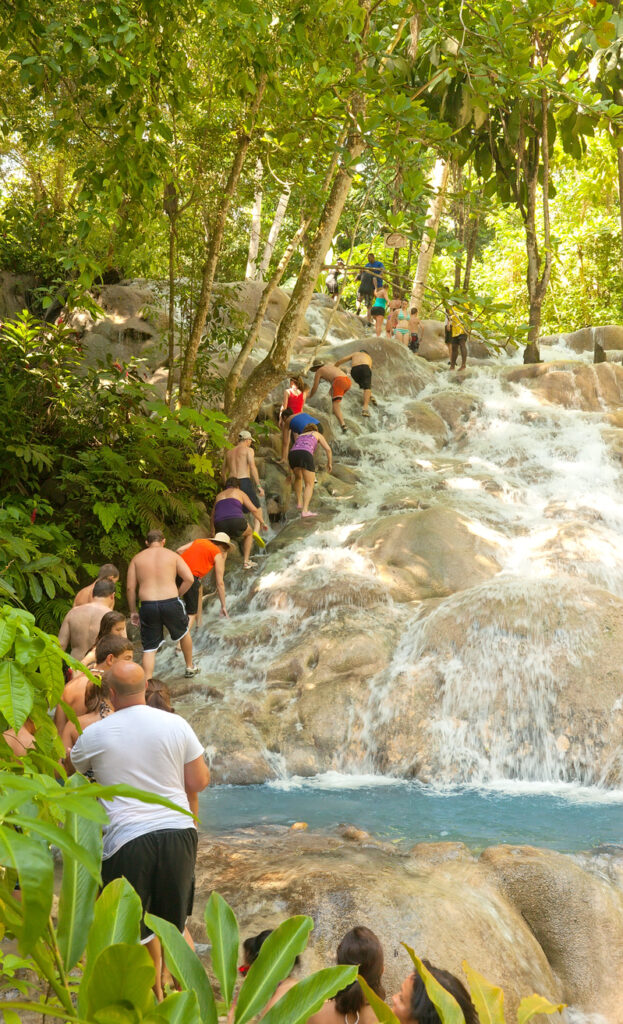 Group of visitors climbing the limestone tiers of Dunn’s River Falls in Ocho Rios, Jamaica, surrounded by lush tropical greenery and flowing water.