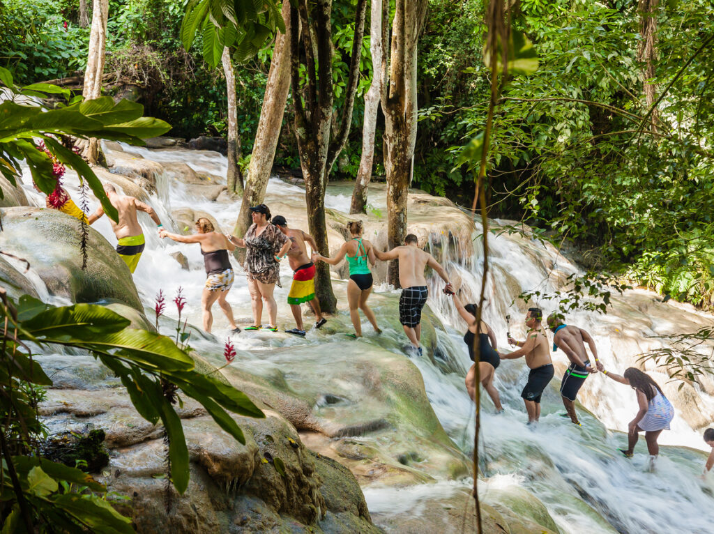 Visitors climbing the terraced limestone steps of Dunn’s River Falls in Ocho Rios, surrounded by lush tropical greenery.