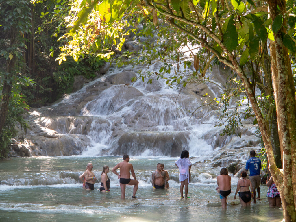 Visitors relaxing in a natural pool at Dunn’s River Falls in Ocho Rios, Jamaica, surrounded by cascading water and lush tropical greenery.