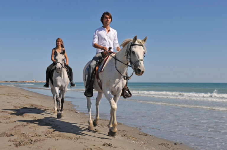 Man and daughter riding horses along a sandy beach with gentle waves in the background during a relaxed coastal trail ride