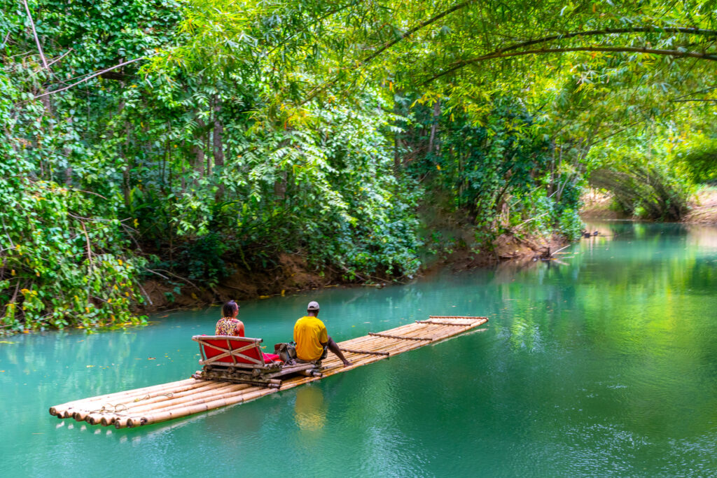 Female tourist and raft captain sitting on a bamboo raft along the Martha Brae River in Falmouth, Jamaica, drifting under a canopy of lush tropical trees