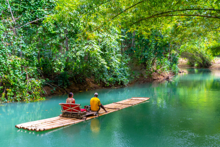 Female tourist and raft captain sitting on a bamboo raft along the Martha Brae River in Falmouth, Jamaica, drifting under a canopy of lush tropical trees