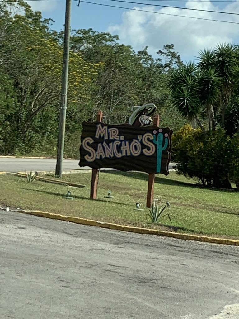 Entrance sign for Mr. Sancho’s Beach Club in Cozumel, featuring colorful lettering and tropical surroundings.