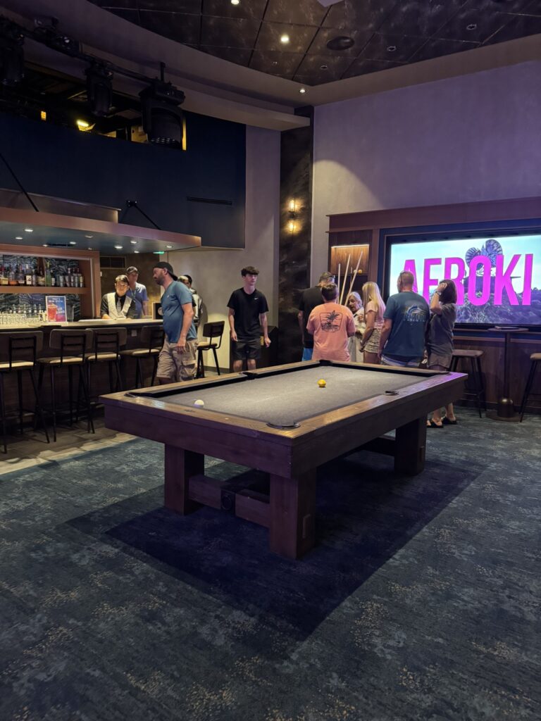 Pool table area inside the Music Hall on Oasis of the Seas, featuring a modern lounge setup with a bar, neon signage, and guests gathered around the table.