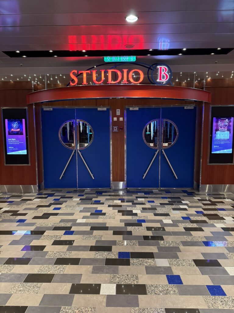 Entrance to Studio B on Oasis of the Seas with blue double doors, digital screens, and signage for the venue where ice‑skating shows take place and guests can skate during designated open‑skate times.