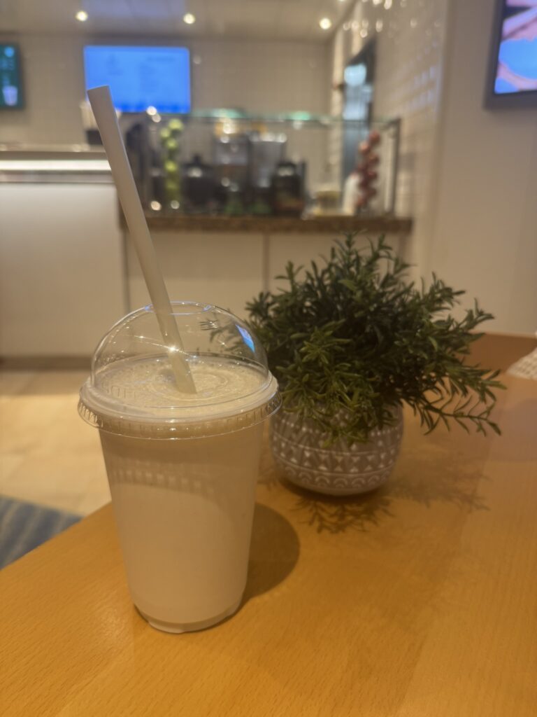 Vanilla smoothie from the spa on Oasis of the Seas, served in a clear cup with a dome lid and straw on a wooden table.