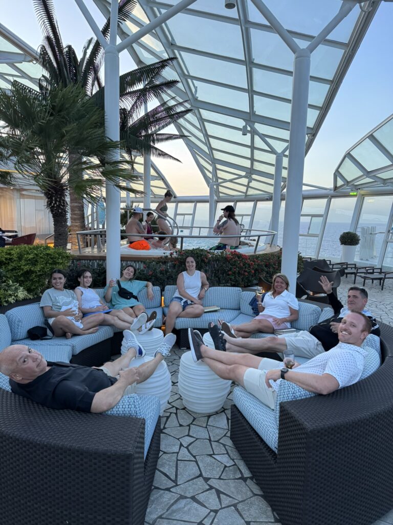 Adults‑only lounge area on Oasis of the Seas with guests relaxing in circular wicker chairs under a glass canopy, enjoying drinks and ocean views.