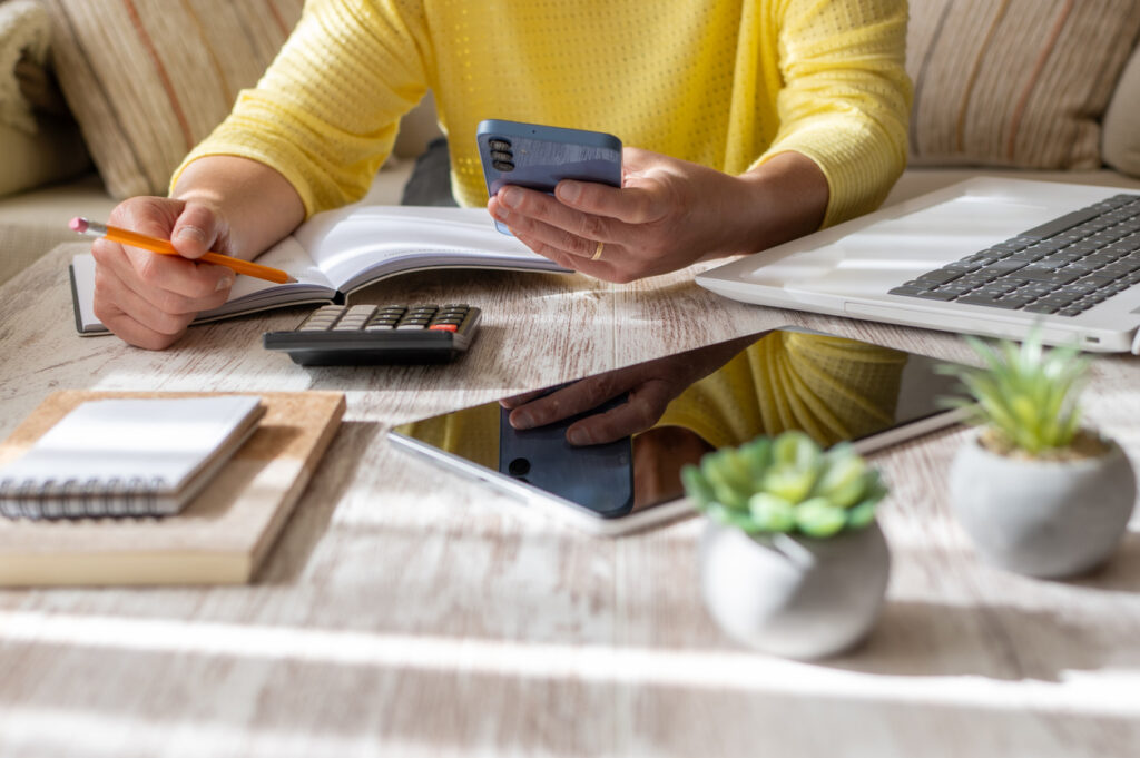 Person working at a desk with a phone, notebook, calculator, and laptop while planning cruise budget and travel style.