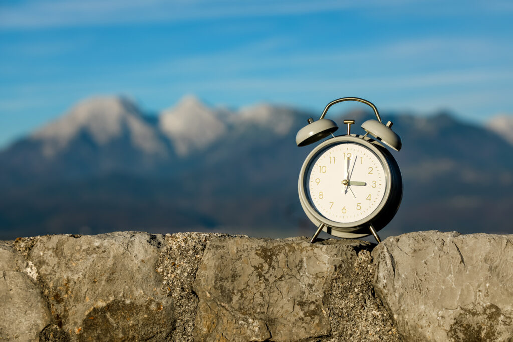 Analog clock outdoors with mountains in the background, symbolizing how cruise time zone changes can affect your schedule.