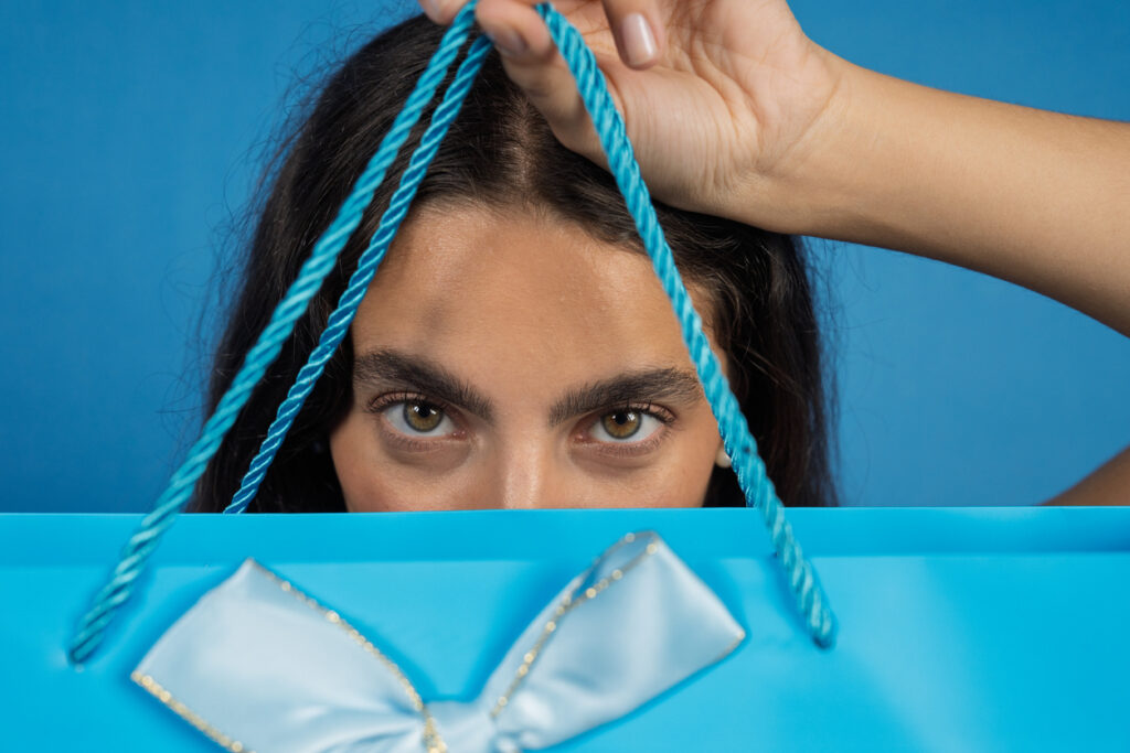 A person holds a bright blue gift bag with a ribbon, creating a fun, eye‑catching moment that hints at the excitement of duty‑free shopping onboard.