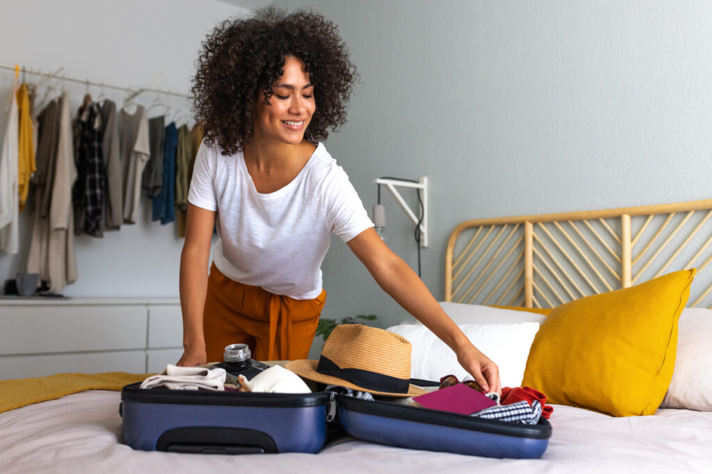 Traveler packing a suitcase on a bed with clothing, a hat, water bottle, and passport, illustrating essentials for a european cruise packing list.