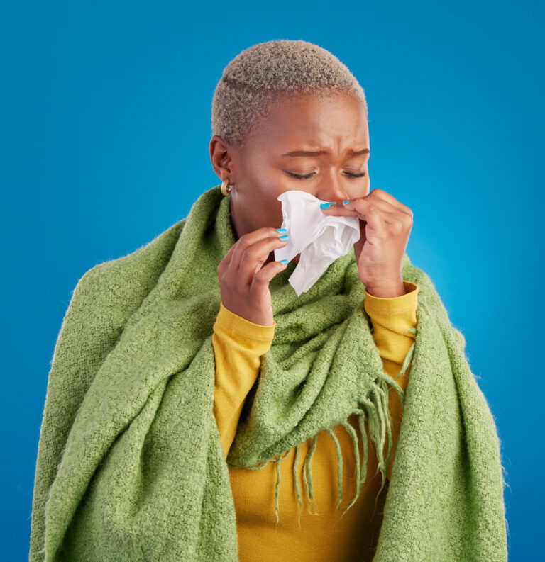 Person wrapped in a blanket and holding a tissue to their nose, illustrating the discomfort of getting sick on a cruise.