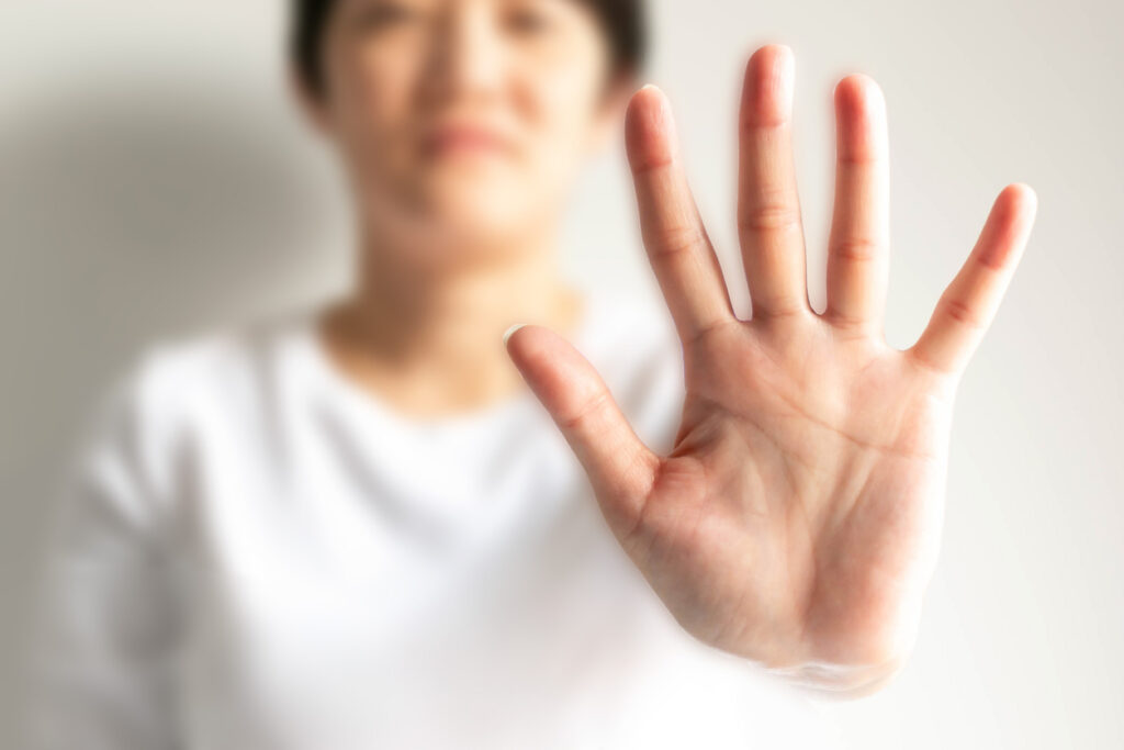 A close‑up of an outstretched hand held toward the camera, palm facing forward, with the person’s face and body softly blurred in the background.
