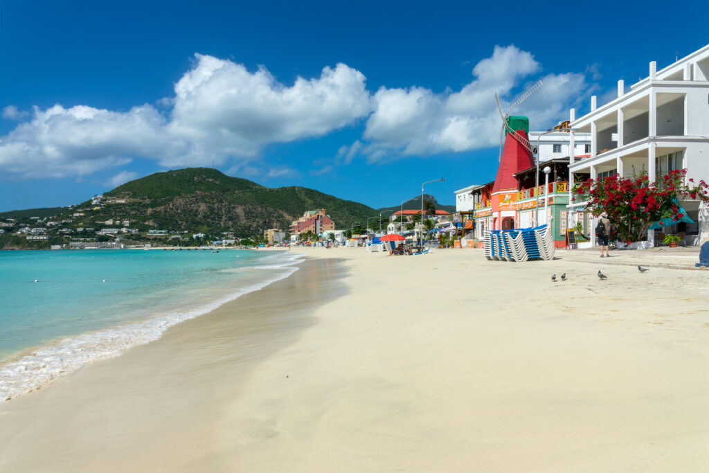 View of Great Bay Beach and the Philipsburg boardwalk on the Dutch side of St. Maarten with clear Caribbean water in the background.