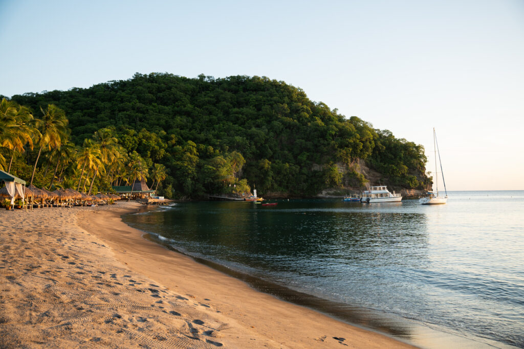 Wide view of Anse Chastanet Bay with dark sand, gentle waves, and tropical greenery along St. Lucia’s southwestern coast.