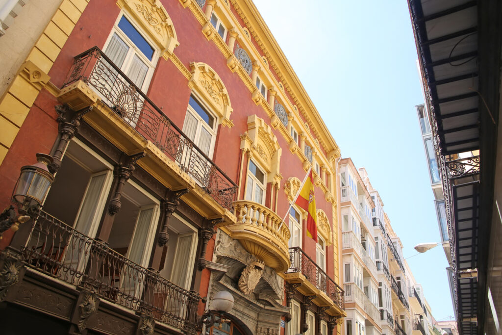 Looking up at the beutiful buildings & architecture lining La Calle Mayor, which is the heart of Cartagena. The street connects Plaza de España with the port. All along, little shops, bars and restaurants., Cartagena, Murcia, Spain.