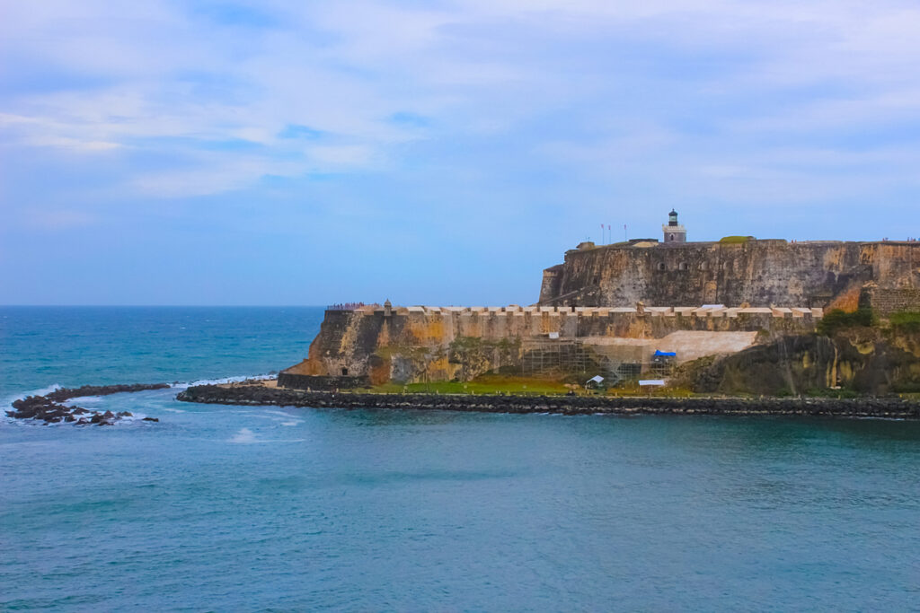 Historic cannon and outer wall of Castillo San Cristóbal in San Juan, Puerto Rico, with a panoramic view of the coastline and a sentry box overlooking the sea.
