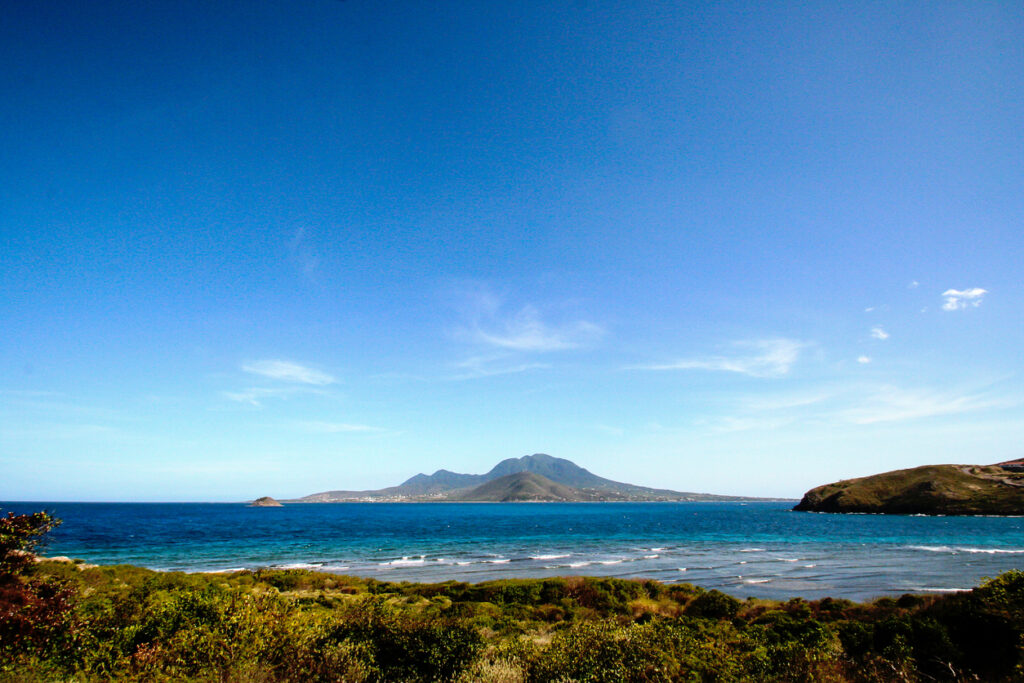 View of Nevis from St. Kitts, with clear blue water and the silhouette of Nevis Peak in the distance.
