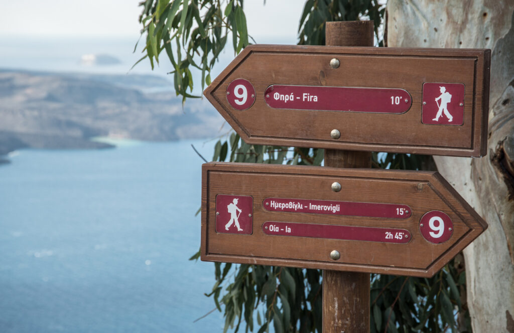 Directional hiking sign along the trail in Fira, Santorini, overlooking the Aegean Sea