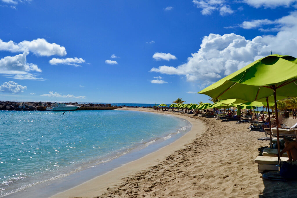 Calm blue water and soft sand at Frigate Bay Beach in St. Kitts, with beach bars and palm trees along the shoreline.