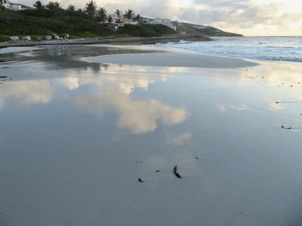 Sunrise at Guana Bay with shallow water reflecting the sky and clouds along the quiet shoreline.