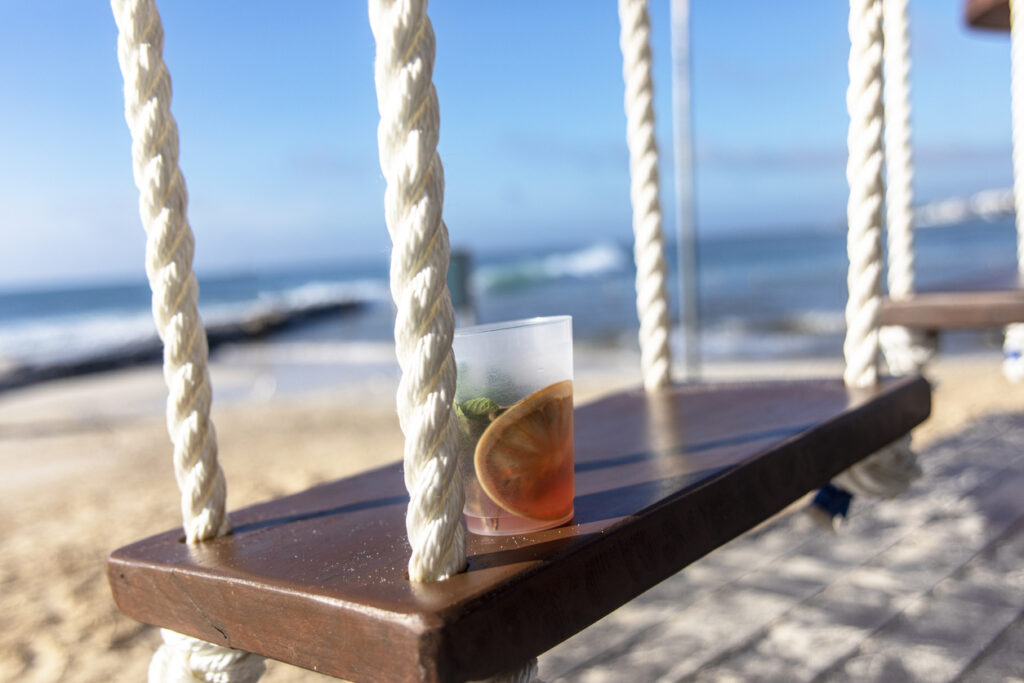 Tropical cocktail resting on a swing with turquoise Caribbean water in the background, capturing the relaxing private‑island vibe of Roatán.