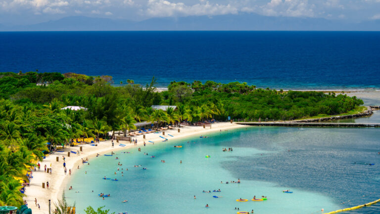 Cruise passengers relaxing on Mahogany Bay Beach in Roatán, Honduras, with calm water and soft sand.
