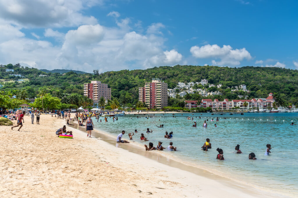 People relaxing on the soft white sand at Ocho Rios Bay Beach in Jamaica, with calm turquoise water and a peaceful Caribbean shoreline.