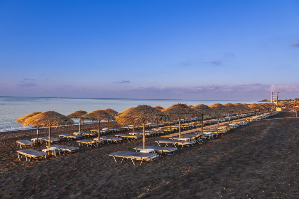 Perivolos beach on Santorini island in Greece at sunrise. The background is a blue sky with white clouds.