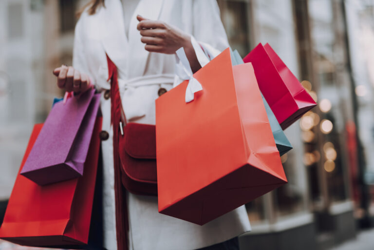 Close‑up of a woman in a white trench coat holding colorful shopping bags, representing a shopping day in San Juan, Puerto Rico.