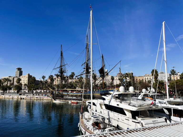 Docked yachts and historic ship in Port Vell, Barcelona, Spain under clear skies