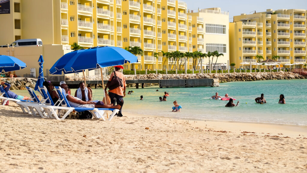 Tourists relaxing on Kim Sha Beach in the Simpson Bay area of St. Maarten, with calm water and coastal views.