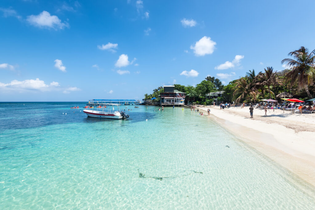 Clear turquoise water and white sand at West Bay Beach in Roatán, Honduras, with palm trees and calm waves.
