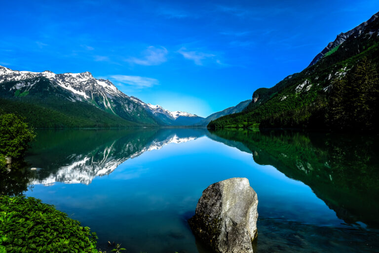 Chilkoot Lake in Haines, Alaska, with its calm turquoise water surrounded by forested mountains and the scenic shoreline of the Chilkat Valley.