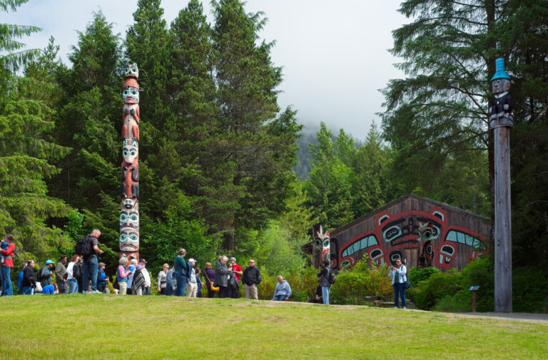 Totem poles and a traditional clan house surrounded by forest at Saxman Native Village in Ketchikan, Alaska.