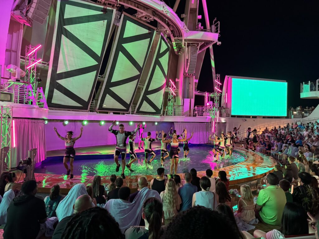 Performers dance and splash across a water stage during a high‑energy nighttime show onboard, showcasing the scale and excitement of cruise entertainment and activities.